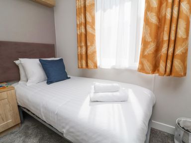 A bedroom with a single bed white bedding towels orange curtains and a bedside table at 16 Manleigh Park in Combe Martin