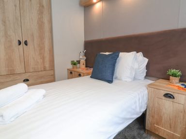A bedroom with a bed with white linens and a blue pillow two wooden bedside tables with plants and a wooden wardrobe at 16 Manleigh Park in Combe Martin