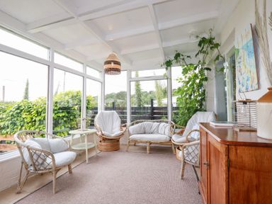 A conservatory with rattan chairs and a table at Nanvivian in Feock near Truro