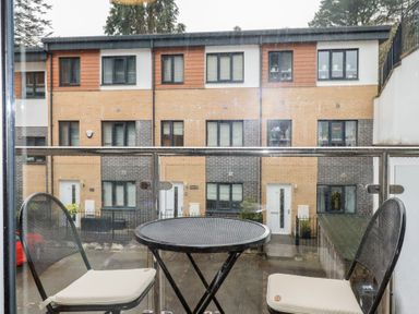 A balcony with a round metal table and two black chairs with white cushions overlooking modern townhouses at 13 Clock Tower Court in Charlestown