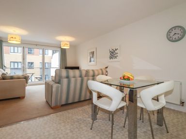 A sitting room with a striped sofa a beige sofa a glass dining table with white chairs and a wall clock at 13 Clock Tower Court in Charlestown