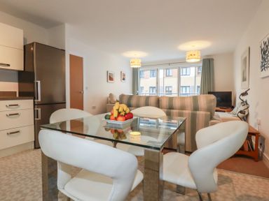 A dining area with glass table and white chairs next to a kitchen and living room at 13 Clock Tower Court in Charlestown