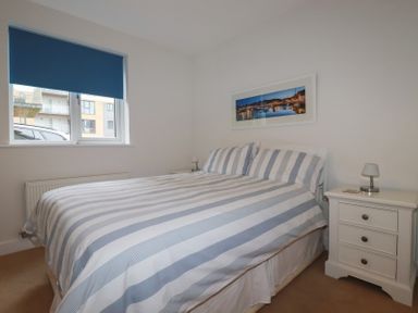 A bedroom with a striped bedspread blue window blind bedside tables and a framed photograph on the wall at 13 Clock Tower Court in Charlestown