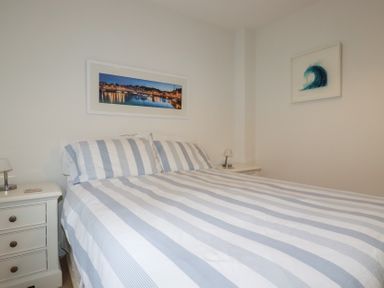 A bedroom with a bed with striped bedding two bedside tables and framed artwork on the walls at 13 Clock Tower Court in Charlestown