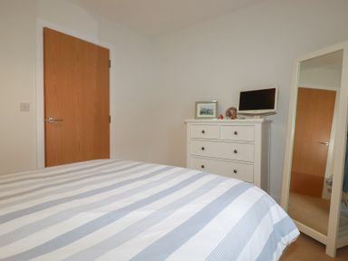 A bedroom with a striped bedspread a white dresser with a small television and a full-length mirror at 13 Clock Tower Court in Charlestown
