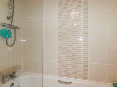 A bathroom with tiled walls a bathtub a showerhead and a glass panel at 13 Clock Tower Court in Charlestown