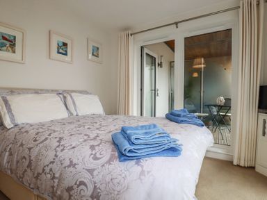 A bedroom with a bed covered in a patterned duvet and blue towels folded on top with framed pictures on the wall and a glass door leading to a balcony at 13 Clock Tower Court in Charlestown