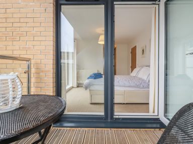 A balcony with a round table and chair overlooking a bedroom with a bed and folded towels at 13 Clock Tower Court in Charlestown