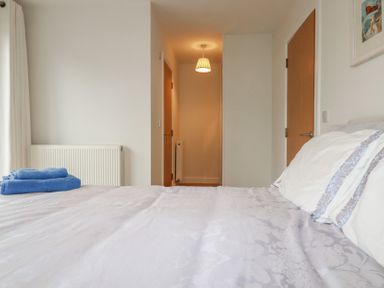 A bedroom with a bed with pillows and folded blue towels on it a radiator next to a window with curtains and two wooden doors at 13 Clock Tower Court in Charlestown