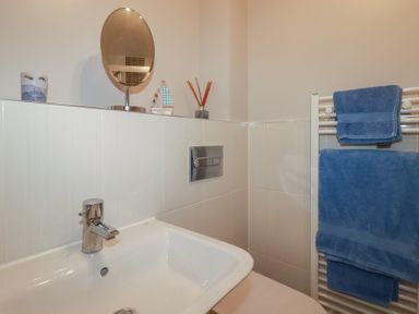 A bathroom sink with a faucet a round mirror and toiletries with blue towels on a heated towel rail at 13 Clock Tower Court in Charlestown