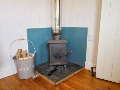 A wood burning stove in a corner with a bucket of kindling and wooden floor at Oak Shepherd Hut in Monkton Wyld near Charmouth