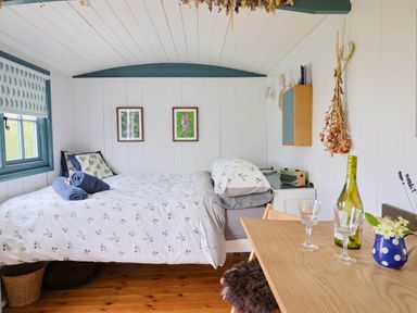 A bedroom with a bed table two glasses a bottle of wine and flowers at Oak Shepherd Hut Monkton Wyld near Charmouth