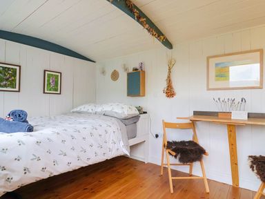 A bedroom with a bed table chair and framed pictures at Oak Shepherd Hut in Monkton Wyld near Charmouth