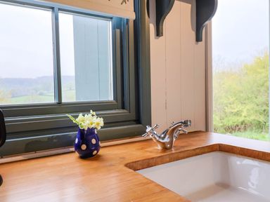 A kitchen sink with chrome faucet a vase with flowers on a wooden countertop near two windows at Oak Shepherd Hut Monkton Wyld near Charmouth