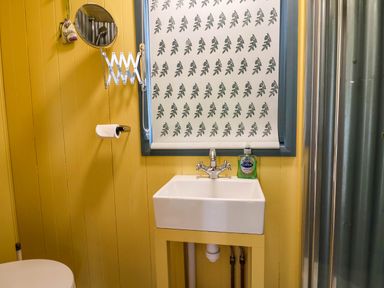 A bathroom with a sink a mirror and a patterned window blind at Oak Shepherd Hut Monkton Wyld near Charmouth