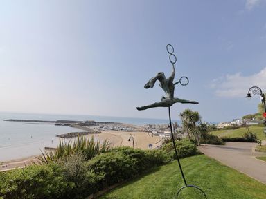 A sculpture of a figure with rings in a park overlooking a beach and marina at Oak Shepherd Hut in Monkton Wyld near Charmouth
