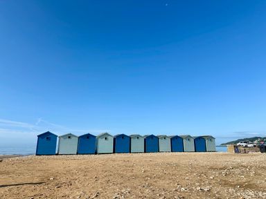A row of beach huts on a sandy shore with a blue sky at Oak Shepherd Hut in Monkton Wyld near Charmouth