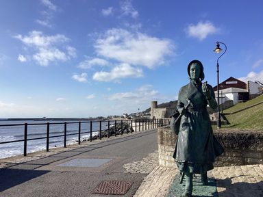 A statue of a woman holding tools near a sea promenade with a building in the background at Oak Shepherd Hut in Monkton Wyld near Charmouth