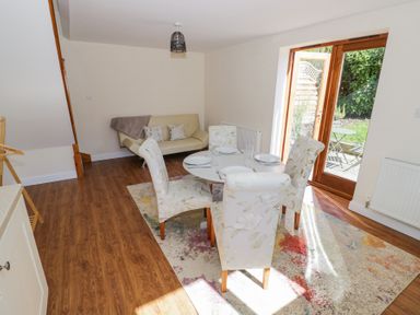 A dining area with a round table set for four and floral chairs next to a sofa and glass doors opening to a garden at Little Barn in Dodwell near Stratford-Upon-Avon