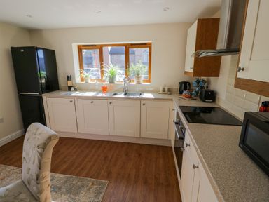 A kitchen with white cabinets a black refrigerator plants on the window ledge and kitchen appliances at Little Barn Dodwell near Stratford-Upon-Avon
