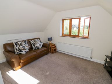 A sitting room with a brown leather sofa cushions side tables lamp a window and carpeted floor at Little Barn Dodwell near Stratford-Upon-Avon
