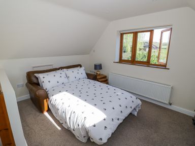 A bedroom with a brown leather sofa bed with white patterned bedding a side table with a lamp and a window at Little Barn in Dodwell near Stratford-Upon-Avon