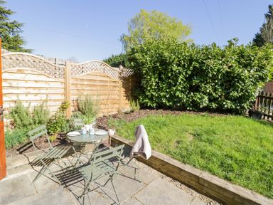 A garden patio with green metal chairs and table next to a grass lawn and wooden fence at Little Barn in Dodwell near Stratford-Upon-Avon