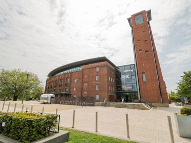 A large brick building with a tall tower and glass entrance of the Royal Shakespeare Company