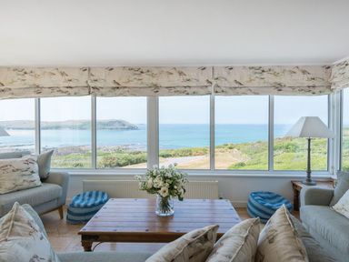 A living room with sofas pillows table lamp and flowers with a sea view at Splits in Daymer Bay