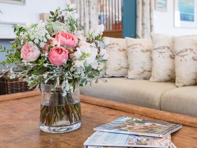 A bouquet of flowers in a glass vase on a wooden coffee table with magazines in a living room at Splits in Daymer Bay