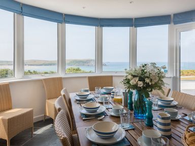A dining room with wicker chairs set with blue and white dishes and a flower vase overlooking the sea at Splits in Daymer Bay