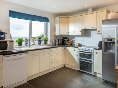 A kitchen with cream cabinets a dishwasher a microwave and a stainless steel fridge at Splits in Daymer Bay