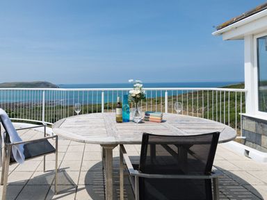 An outdoor patio with a wooden table chairs wine glasses and a bottle overlooking the sea at Splits in Daymer Bay