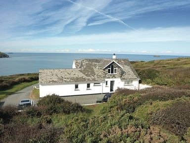 A white house with a gray tiled roof near the sea surrounded by shrubs at Splits in Daymer Bay