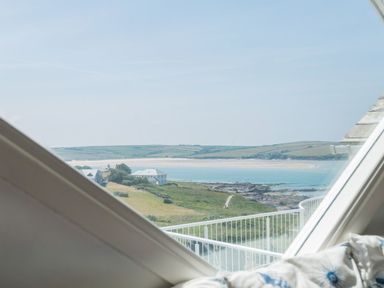 A coastal landscape with houses green hills and ocean seen through a window at Splits in Daymer Bay