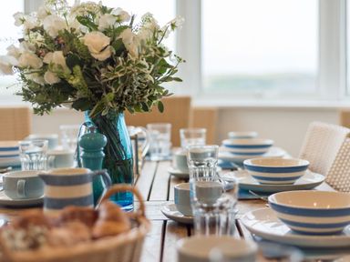 A dining table set with bowls plates cups glasses and a blue vase with flowers at Splits in Daymer Bay