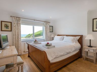 A bedroom with a wooden bed and white bedding next to a window with floral curtains at Splits Daymer Bay
