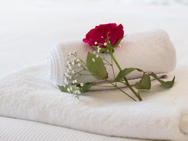 A rolled white towel on top of a folded white towel with a red rose and white flowers on a bed at Splits in Daymer Bay