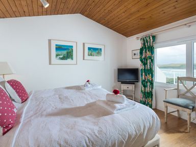 A bedroom with a double bed two framed pictures on the wall and a window with floral curtains at Splits in Daymer Bay