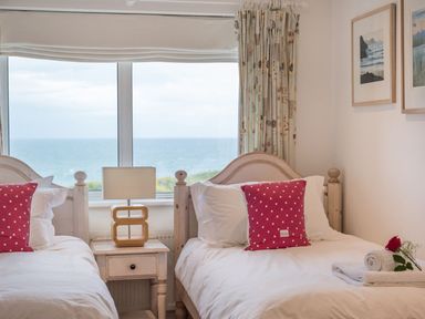 A bedroom with two single beds white bedding red pillows and a window with ocean view at Splits Daymer Bay