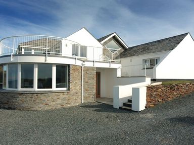A modern house with white walls stone facade and a balcony at Splits in Daymer Bay