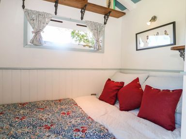 A small bedroom with a bed with red pillows and floral quilt under a window with patterned curtains and a framed bird picture on the wall at Songbirds in St Michaels Kent