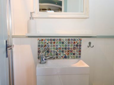 A small bathroom sink with a silver faucet colorful tiled backsplash white soap dispenser and a mirror at Songbirds in St Michaels Kent