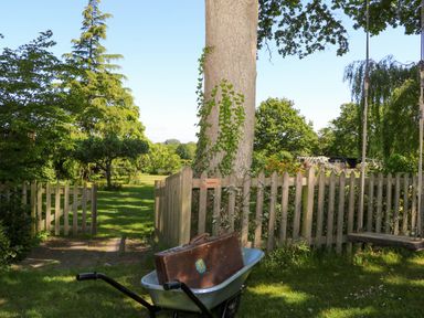 A garden with a wheelbarrow holding a suitcase near a wooden fence and a tree with a swing at Songbirds in St Michaels Kent
