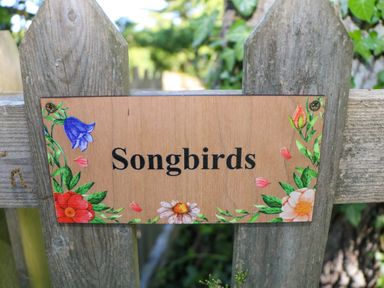 A wooden fence with a sign that says Songbirds surrounded by flowers at Songbirds in St Michaels Kent
