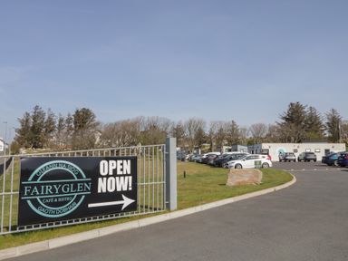 A parking lot with cars and a building and a sign for Fairyglen Cafe and Bistro at Gleann Na Siog in Gaoth Dobhair