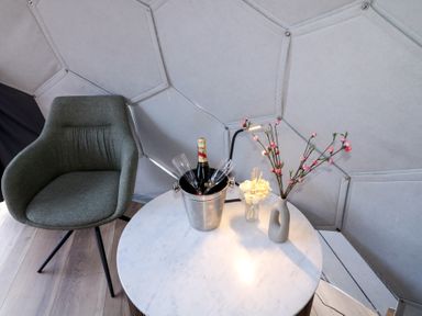 A round marble table with a champagne bucket holding a bottle and two glasses a small lamp and two vases with flowers next to a green chair at Number 1 Dome in Derrybeg County Donegal
