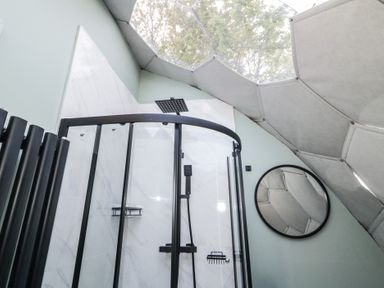 A bathroom with a glass shower enclosure under a geometric dome ceiling with a round mirror on the wall at Number 1 Dome in Derrybeg County Donegal