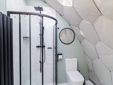 A bathroom with a glass shower enclosure a toilet and a round mirror on the wall at Number 1 Dome in Derrybeg County Donegal