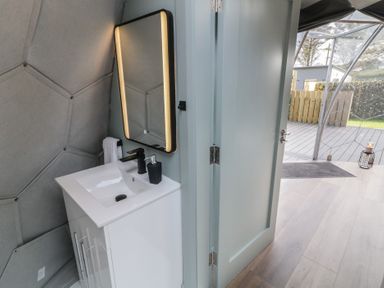 A bathroom sink with a mirror and soap dispenser next to an open door leading to an outdoor deck at Number 1 Dome in Derrybeg County Donegal